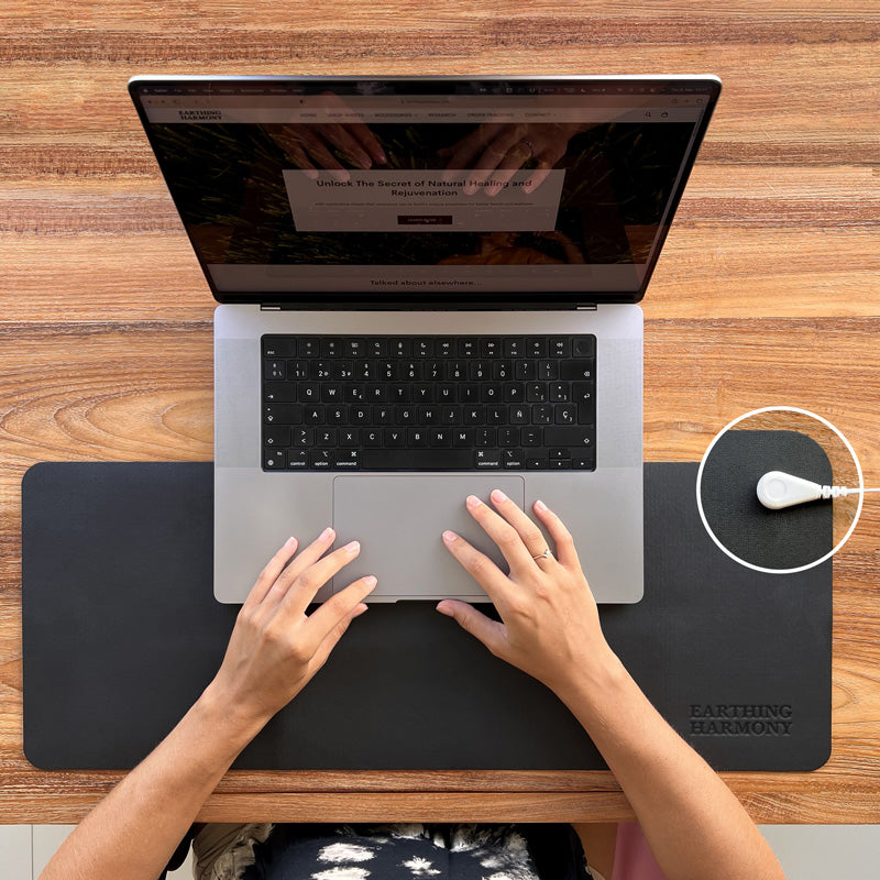 Frau arbeitet an einem MacBook Pro-Computer und schützt sich vor EMF mit einer Erdungsmatte, die auf einem natürlichen Holzschreibtisch platziert ist